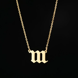 Détail macro du pendentif lettre m gothique sur une chaîne à maillons en acier doré