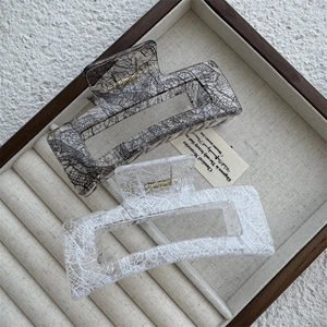 Detail of square lace-textured resin hair claws in a wooden box with metal springs