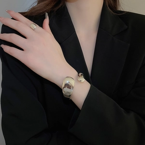Close-up of polished gold wide cuff bracelet and matching ring on a black suit sleeve