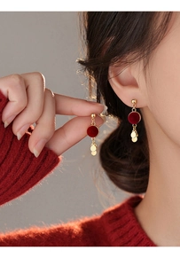 Detailed close-up of velvet red round stud earrings with golden tassel discs on a model