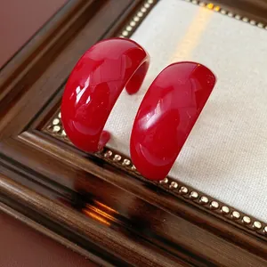 Vintage red C-shape resin hoop earrings with glossy finish on a textured background