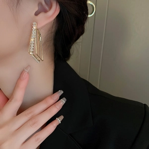 Close-up of geometric gold drop earrings with white zircons on a fashion model