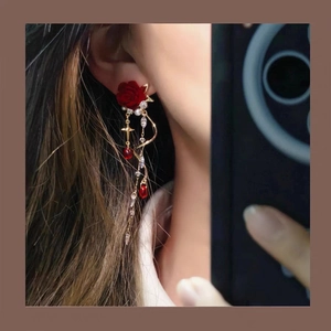 Detail of red rose stud earrings with velvet texture and golden fringe on a model