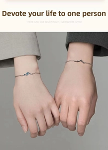 Detailed view of silver mountain and wave charms on couple bracelets worn by hands