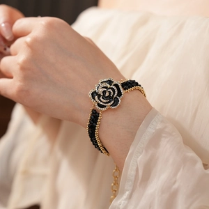 Close-up of black rose bracelet with diamond edges and gold chain on model's wrist