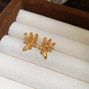 Macro shot of 24K gold plated flower stud earrings with zircons on beige velvet base