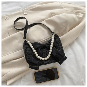Detail of black lace handbag with large satin bow and elegant pearl handle strap
