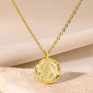 Macro shot of gold constellation coin pendant with zircons on soft linen fabric background