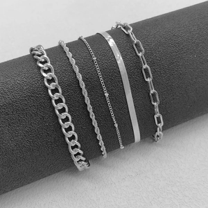 Detail of silver Figaro, Cuban, and snake chain bracelet set on a textured display