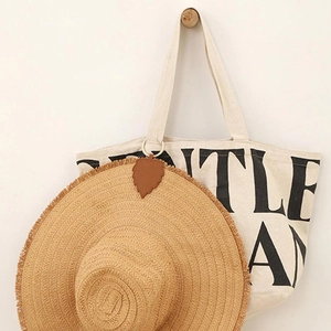 Close-up of cream canvas tote with black lettering and summer straw hat on wall hooks