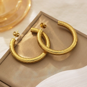 Macro shot of large gold C-shaped hoop earrings with hammered texture on jewelry stand