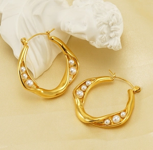 Detail of French vintage irregular gold hoop earrings with pearls on beige texture