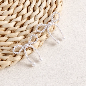 Detail of handmade woven pearl bow earrings with elegant white fringe and glossy finish