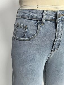 Detail van een lichtblauwe jeans met hoge taille, stiksels en knoopsluiting getoond
