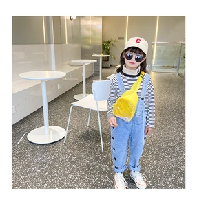 Detail of yellow transparent PVC duck bag and kids striped shirt with denim overalls