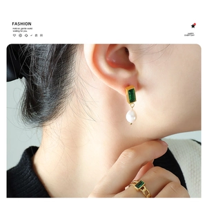 Detail of vintage emerald zircon and pearl earrings with matching chain ring on model