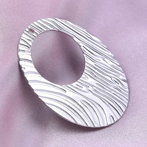 Macro shot of silver 304 stainless steel oval pendant with wavy texture on pink satin