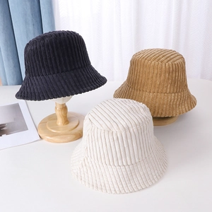 Detailed texture of corduroy bucket hats in black, khaki, and cream on wooden stands