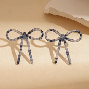 Detailed view of blue and white striped acetate bow earrings on a textured stone surface
