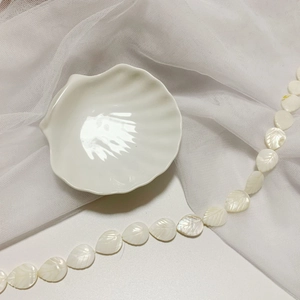 Close-up of leaf-shaped natural shell beads with glossy finish on a white ceramic shell tray