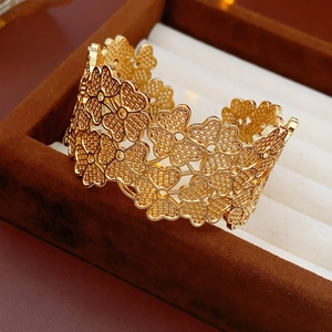 Macro detail of the golden open cuff bracelet with hollow four-leaf clover flower patterns
