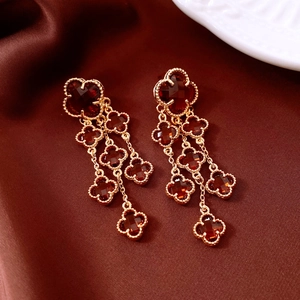 Close-up of vintage 18k gold plated quatrefoil tassel earrings with red glass gems
