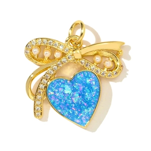 Macro detail of heart pendant with blue opal inlay, gold bow and pearl accents