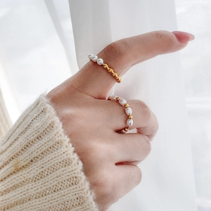 Detail of freshwater pearl and gold bead crossover ring worn on hand with knit sweater