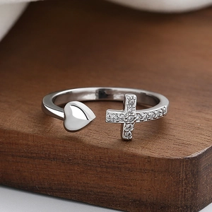 Silver open ring with cross and heart motifs set with zircon on wooden surface