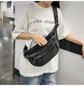 Close-up of black washed denim crossbody chest bag with adjustable strap on white T-shirt