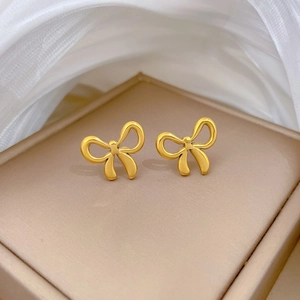 Elegant gold bow earrings on beige jewelry box with soft white silk background