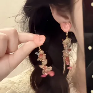 Close-up of pink heart stud and colorful irregular stone long tassel earrings on a model