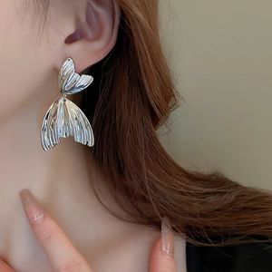 Detailed view of silver fishtail earrings with metallic pleated texture on model