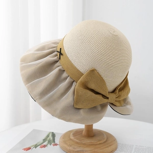 Elegant wide-brim straw hat with a large bow and ribbon detail on a wooden stand