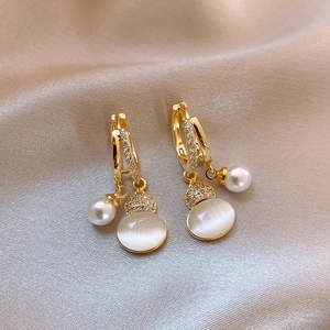 Close-up of gold hoop earrings with sparkling zircons, white pearl and cat eye stone