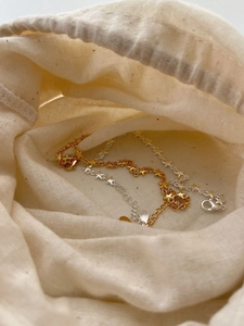 Detailed view of silver and gold star charm bracelets in a beige cotton drawstring pouch
