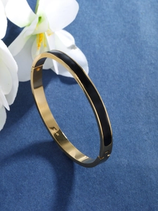 Detailed view of a gold-plated bangle with black enamel stripes on a blue textured background