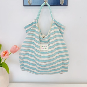 Close-up of blue striped canvas tote bag with woven label on minimalist wall hook