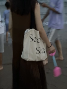 Detail of minimalist cream canvas tote bag with See Sea text print on a beach