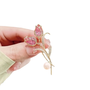 Elegant gold tulip brooch with pink gemstone petals and pearl detail held by hand