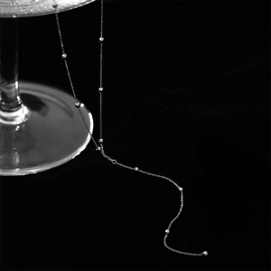 Detailed close-up of a silver tassel necklace draped on glass with a black background