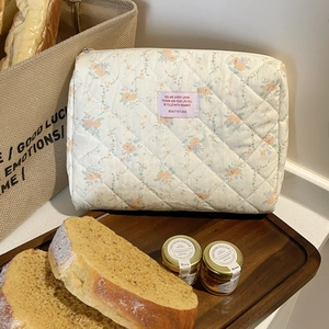 Close-up of quilted floral makeup bag with pink woven label on a wooden tray