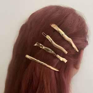 Set of four gold irregular molten metal hair clips on a model against white background