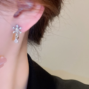 Detailed view of silver snowflake earrings with zircon drop pendant on a model's ear