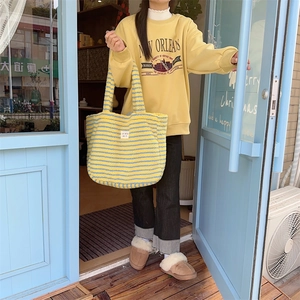 Outdoor shot of a woman carrying a fuzzy yellow striped tote bag with a matching hoodie