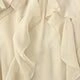 Vue détaillée d'une blouse en satin beige montrant des volants et la texture lisse du tissu