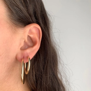 Close-up of gold stainless steel thick hoop earrings set worn on ear for women