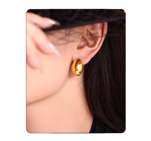 Close-up of model wearing oval gold polished titanium steel hoop earrings with glossy finish