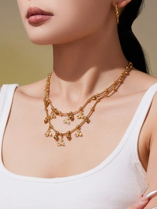 Detail van gouden dubbellaagse ketting met vlinder- en hartbedeltjes gedragen door model
