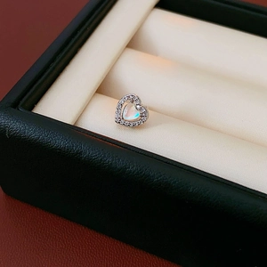 Macro view of heart-shaped silver earrings with moonstone and pavé zircon on a beige cushion